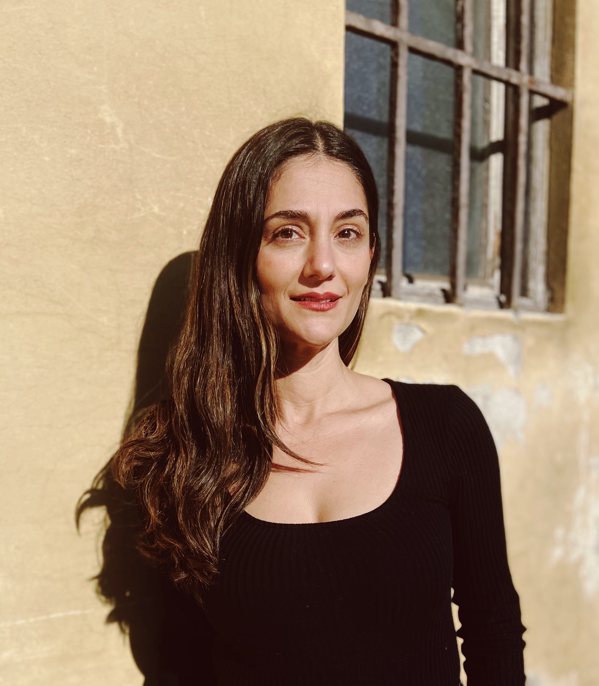 Headshot of Vera Kachouh in a black shirt standing against a tan wall.